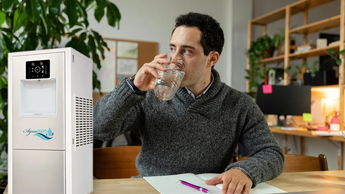 Hombre bebiendo agua junto a un generador AguaPARS BRISA en su oficina